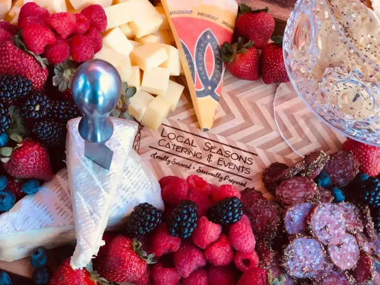 Assorted berries, cheese cubes, and snacks arranged on a tray with a napkin and metallic spoon around a card.