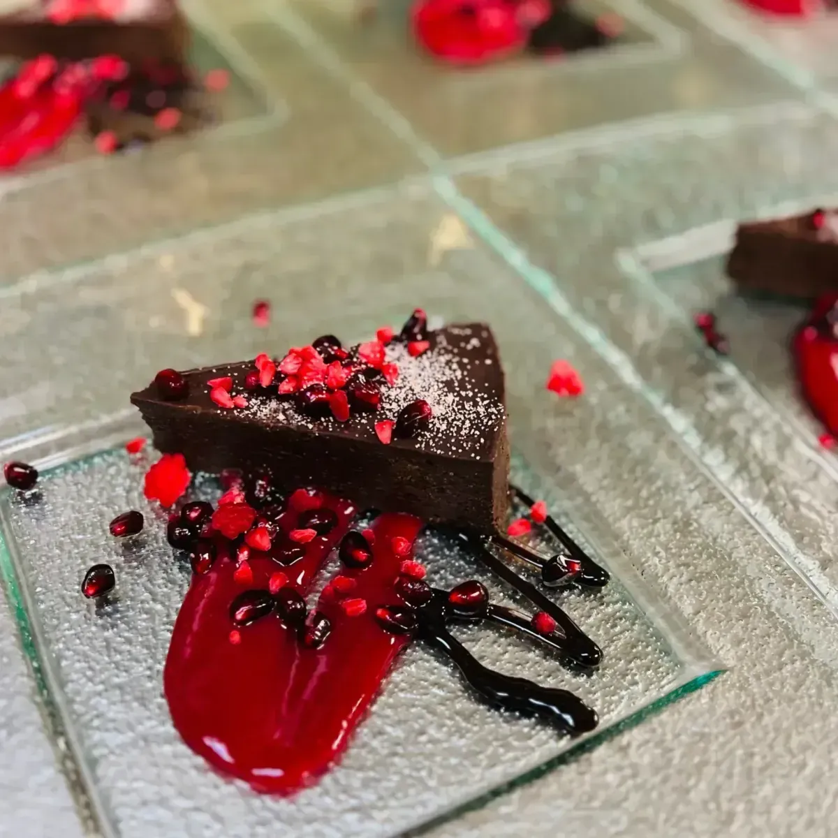 Chocolate dessert slice with red berry sauce and scattered raspberry pieces on a glass plate