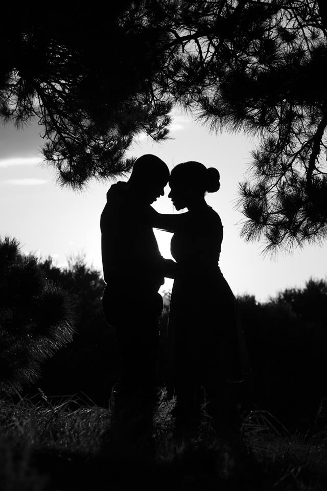 A silhouette of a man and woman hugging under a tree.
