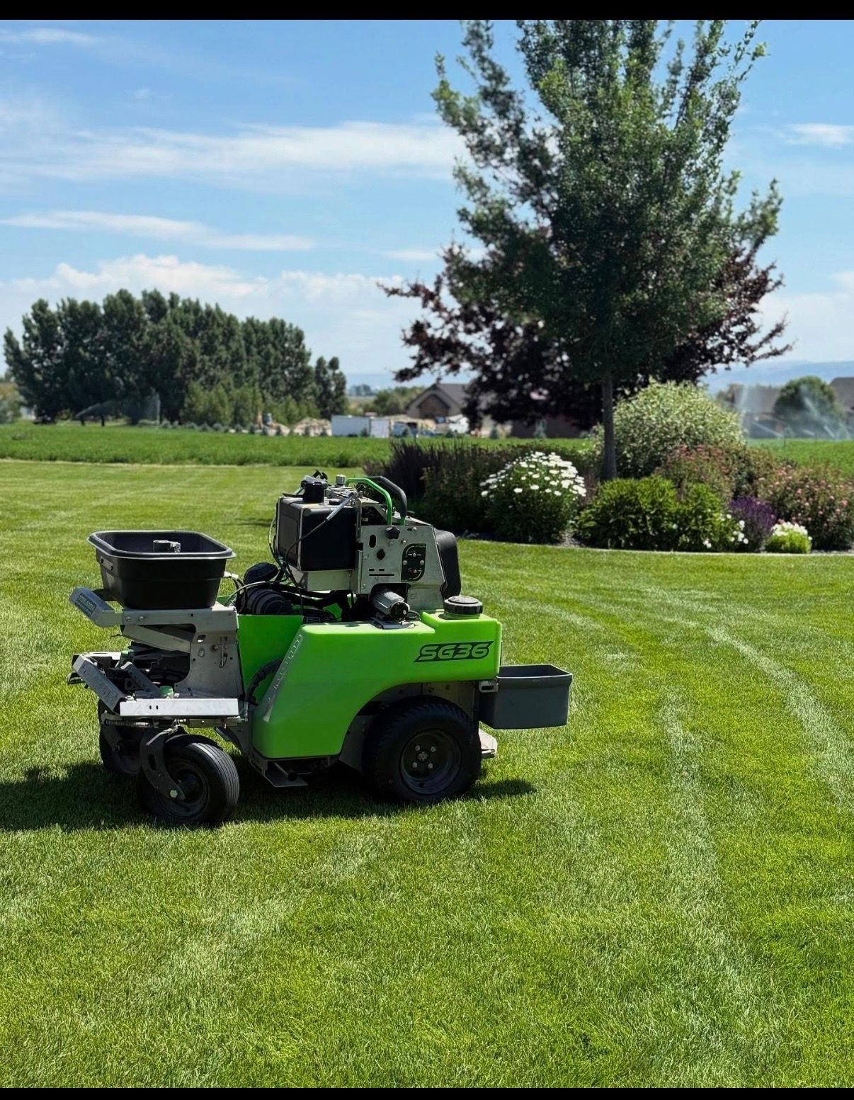 Green lawn mower parked on a manicured grassy field with trees and shrubs in the background
