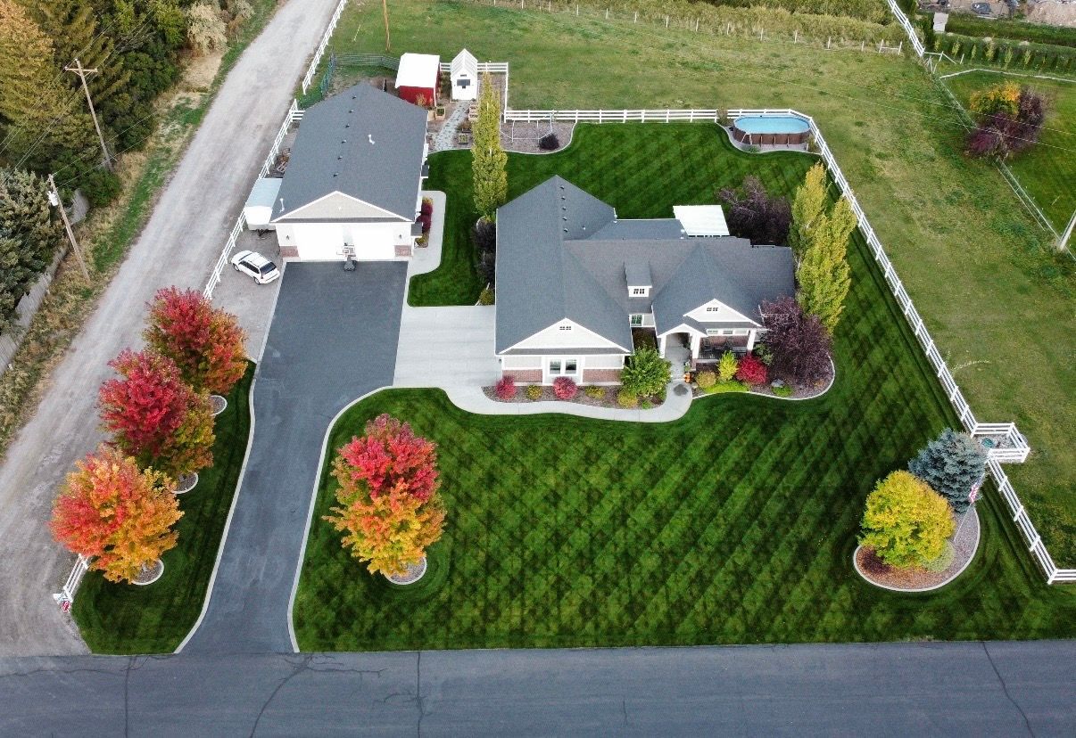 Aerial view of a suburban house with a driveway, garage, and neatly landscaped lawn bordered by autumn trees.