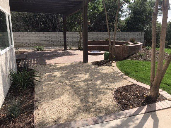 Backyard patio with pergola, gravel, brick seating area, and lush green lawn.