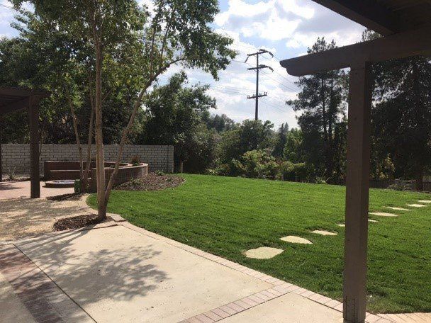 Lawn with stepping stones, patio, and trees viewed from under a covered patio.