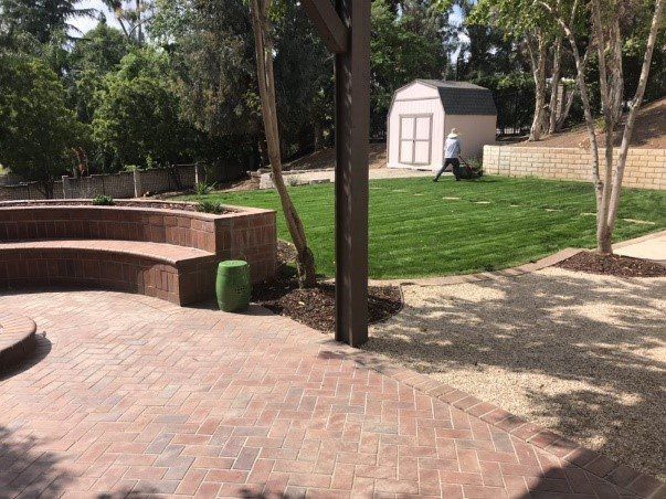 Brick patio with terraced seating, leading to a grassy yard with a shed and a person.