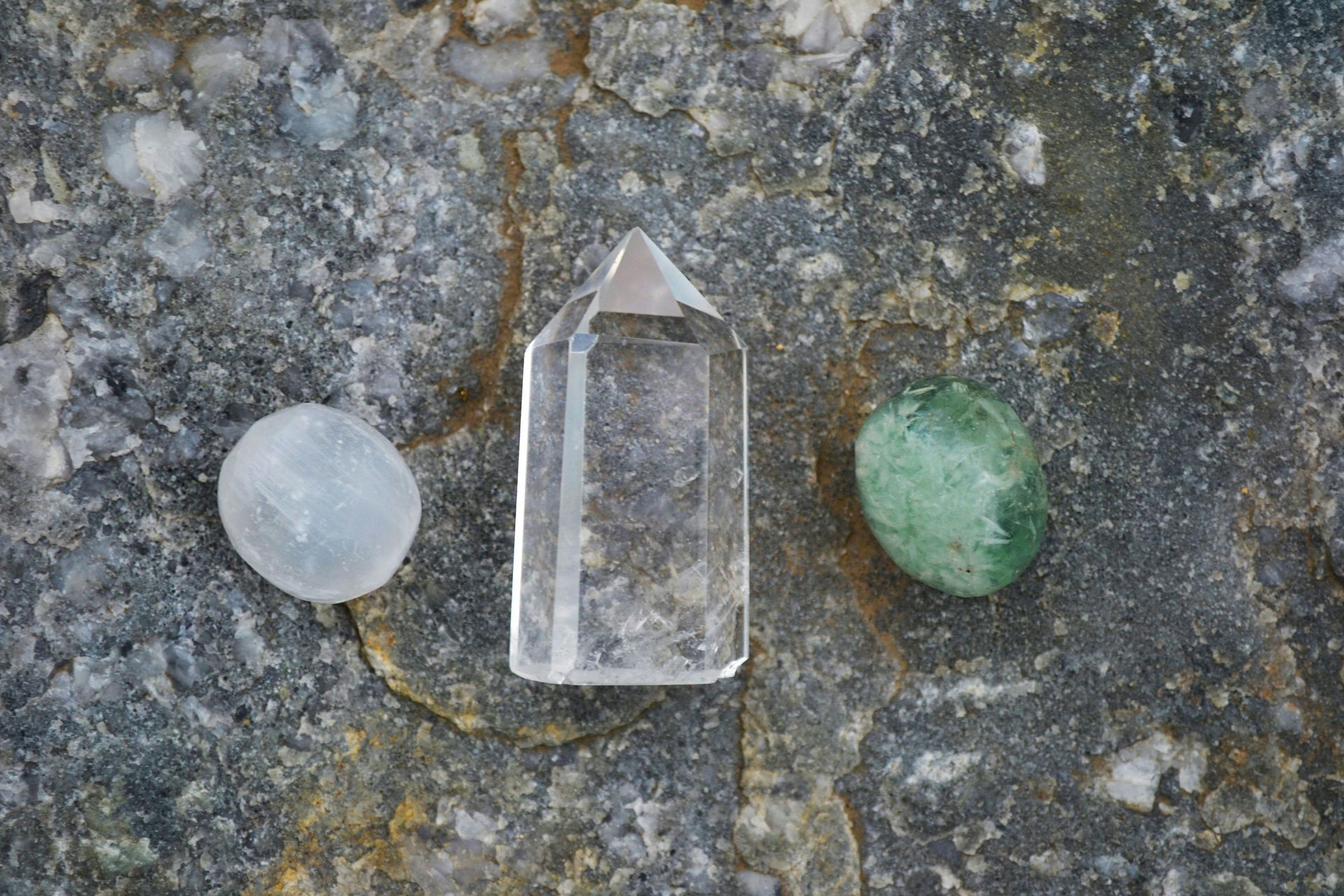 A clear crystal and a green crystal are sitting on a rock.
