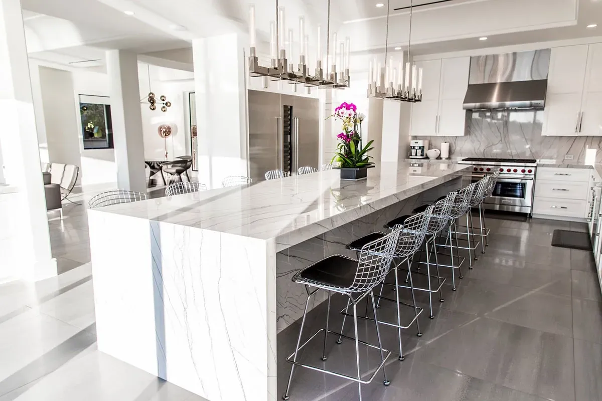 A kitchen with white cabinets , stainless steel appliances , a long island and stools.