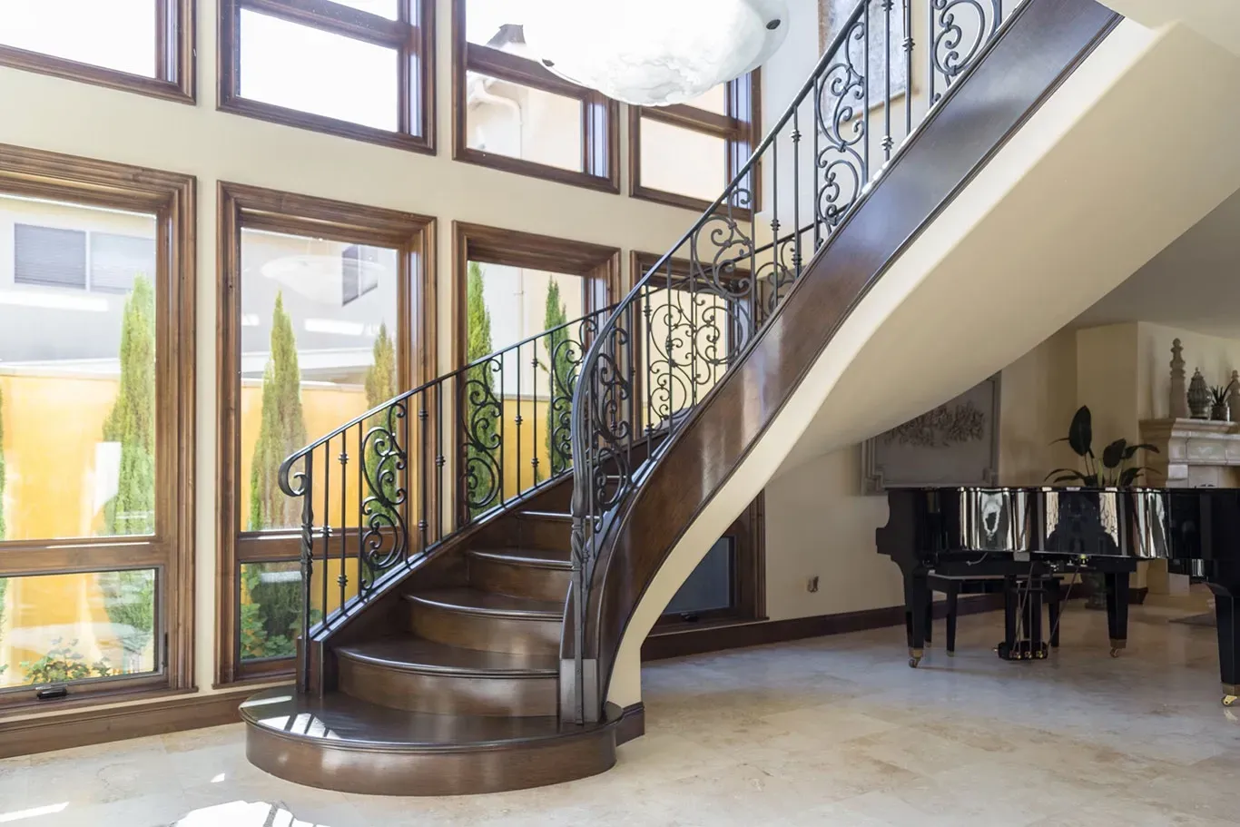 A wooden spiral staircase with a wrought iron railing in a living room with a piano.