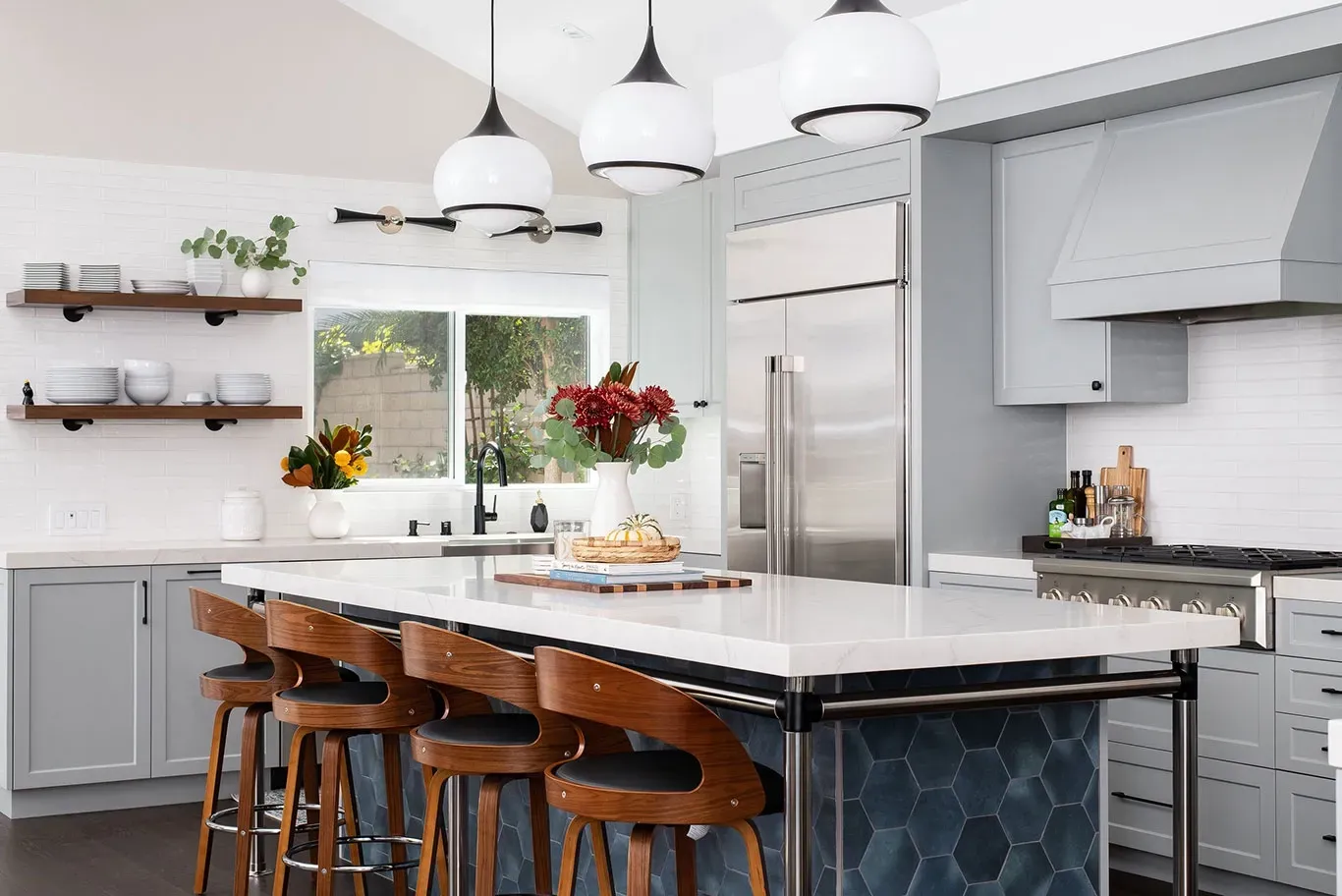 A kitchen with a large island , stools , a refrigerator and a sink.