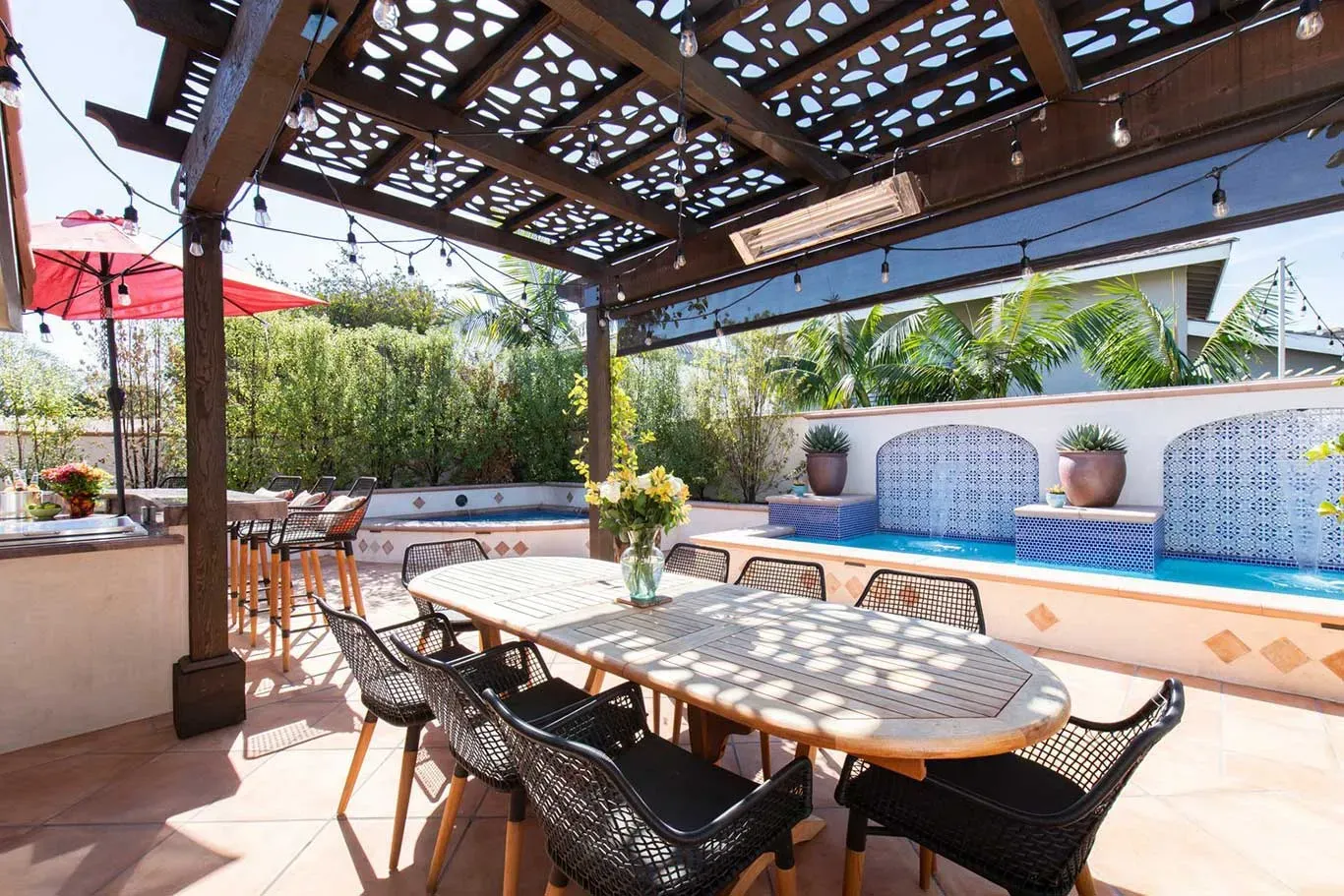 A patio with a table and chairs under a pergola next to a pool.