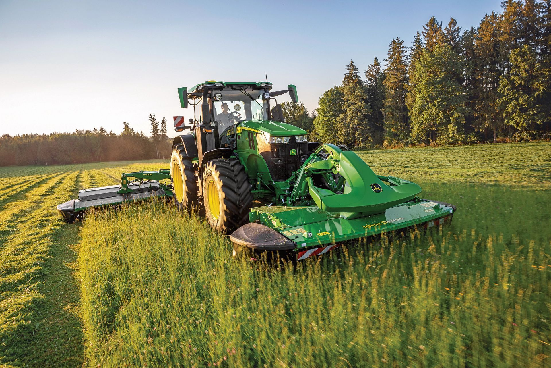 A green tractor is cutting grass in a field.