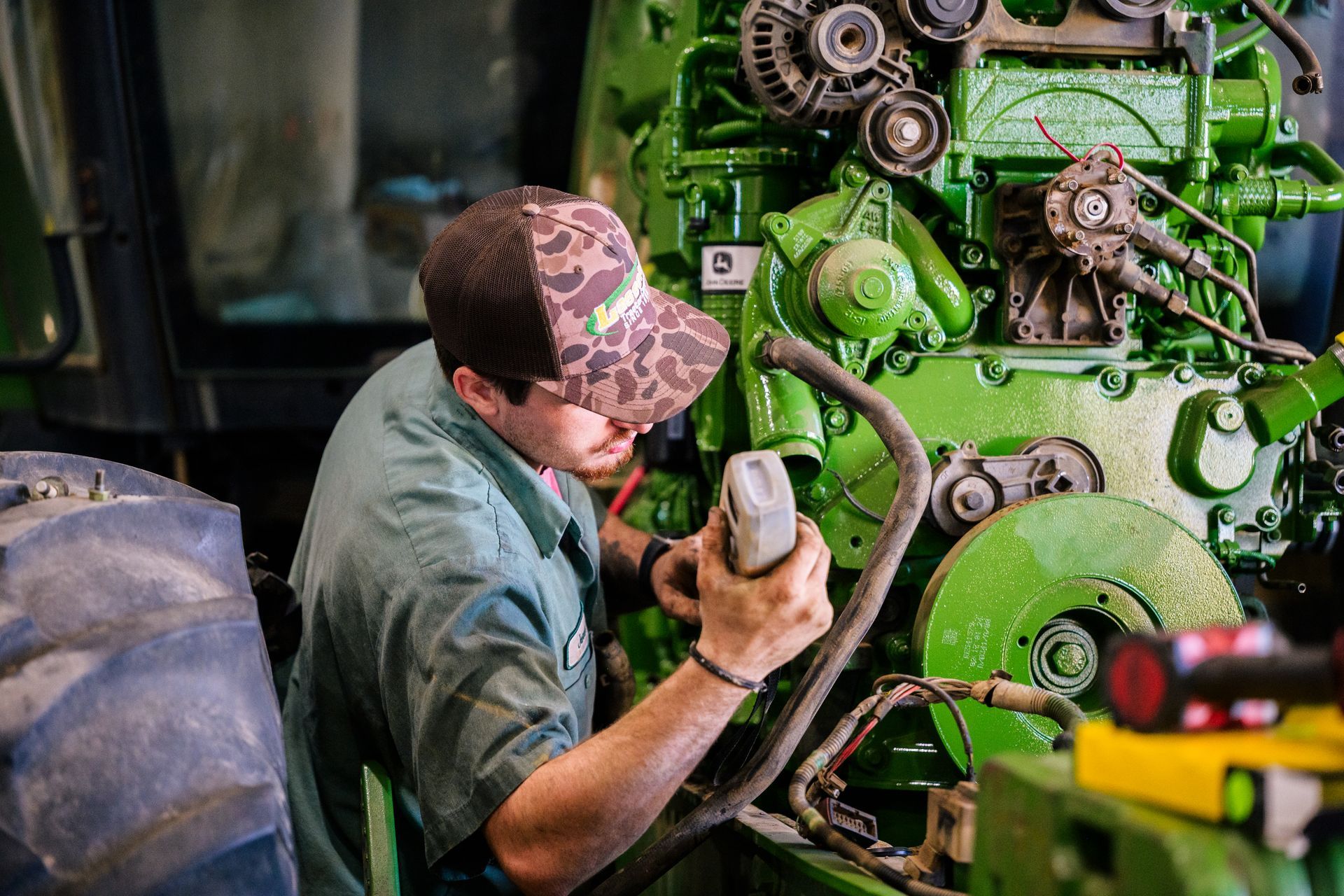 A man is working on a green tractor in a garage.