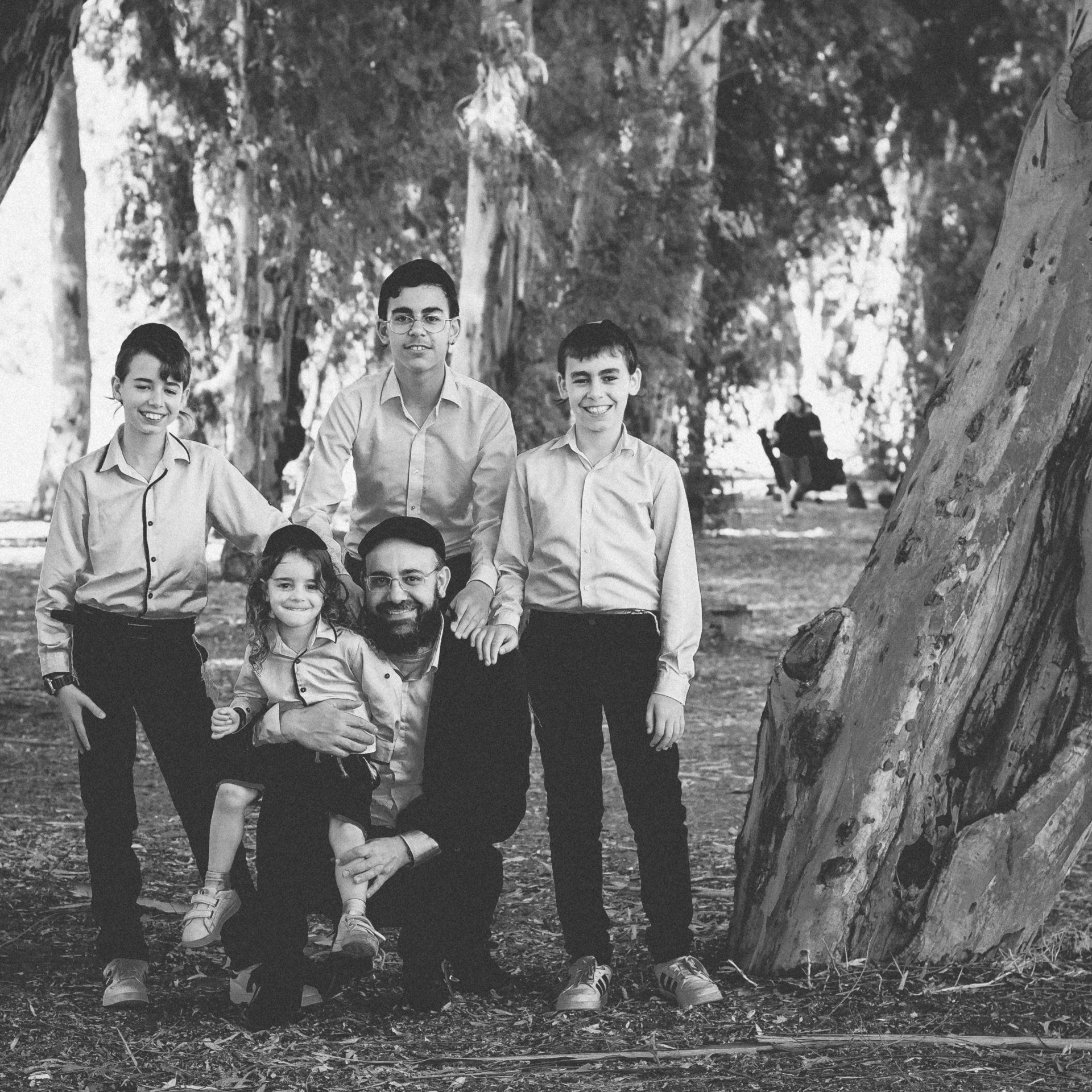 משפחה מביטה למצלמה בצילומי משפחה בחורשה, תמונה בשחור לבן