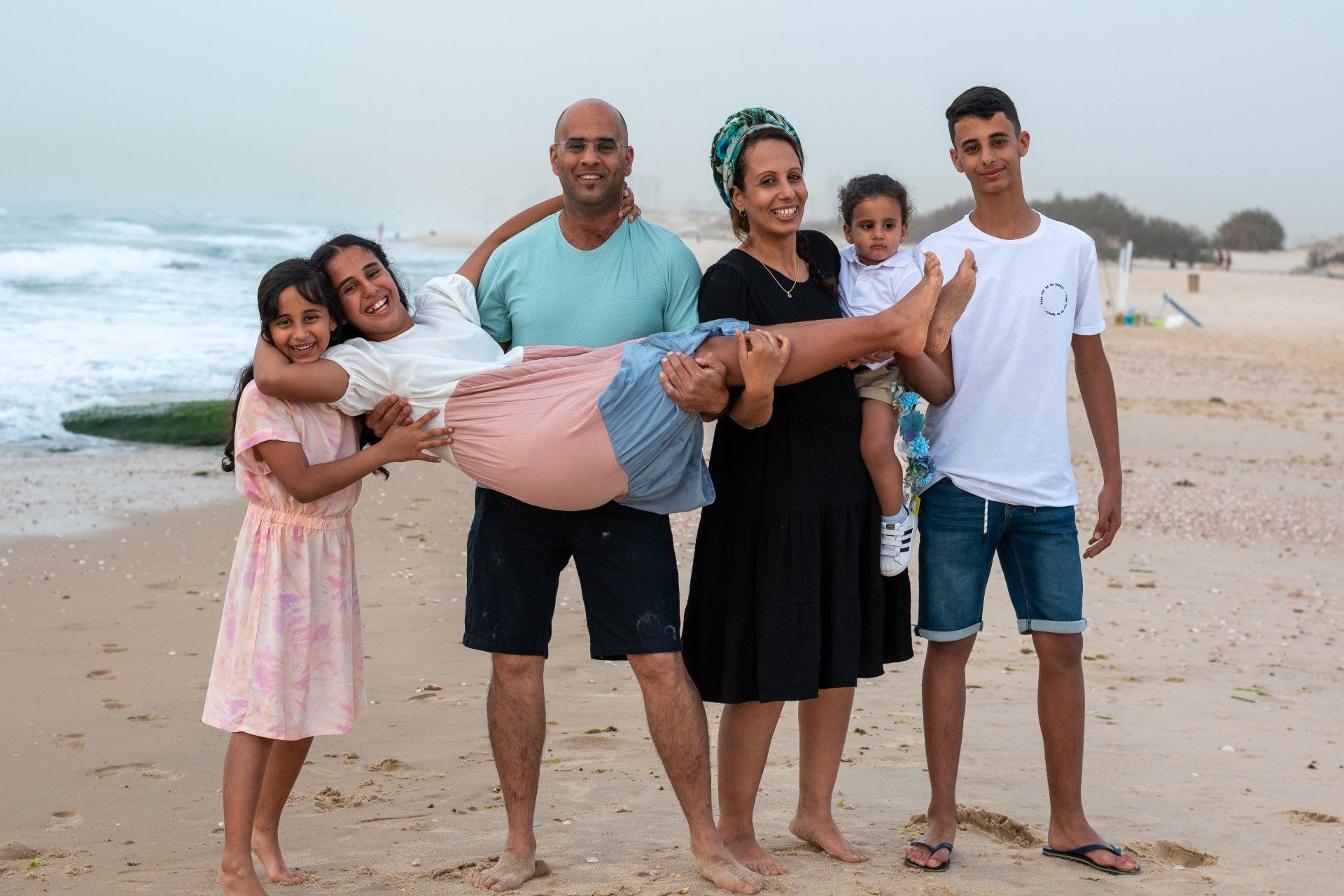 משפחה חמודה מחזיקה לאורך את בת המצווה על רקע חוף הים בצילומי משפחה בטבע