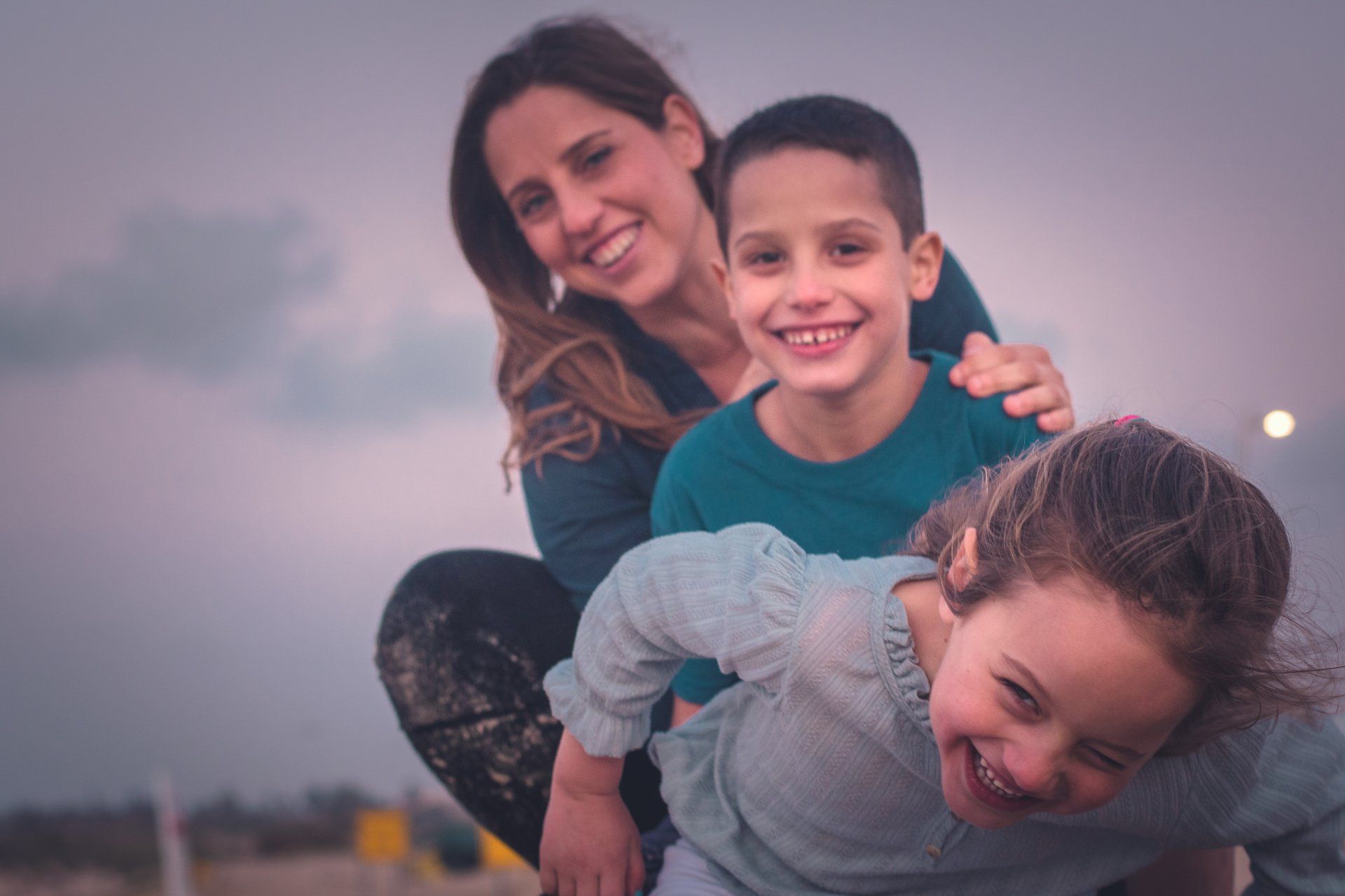 אמא ושני ילדים צוחקים אל מול המצלמה בצילומי משפחה
