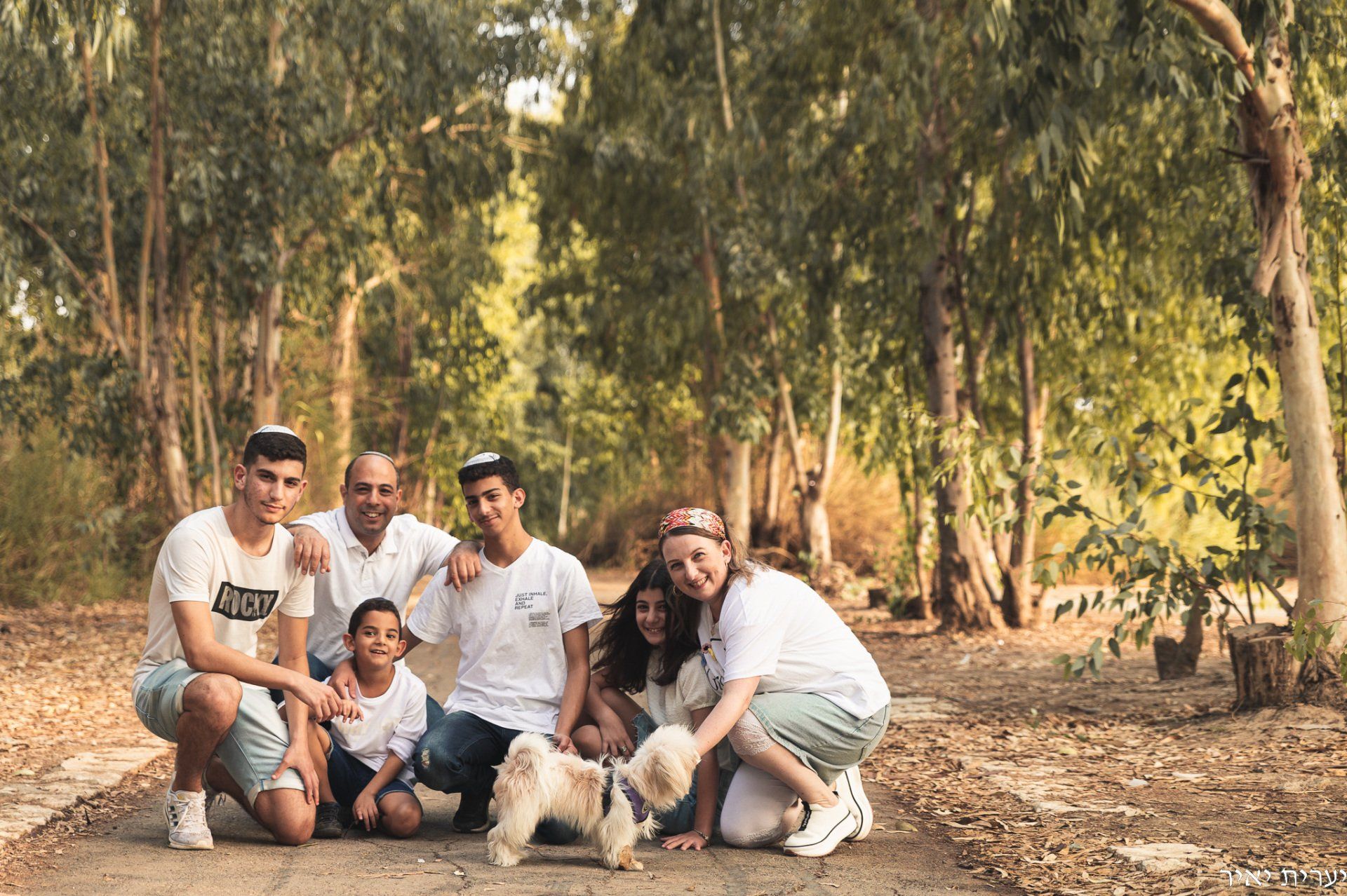 משפחה מתוקה יושבת עם הכלב ומביטים למצלמה בצילומים בחורשה