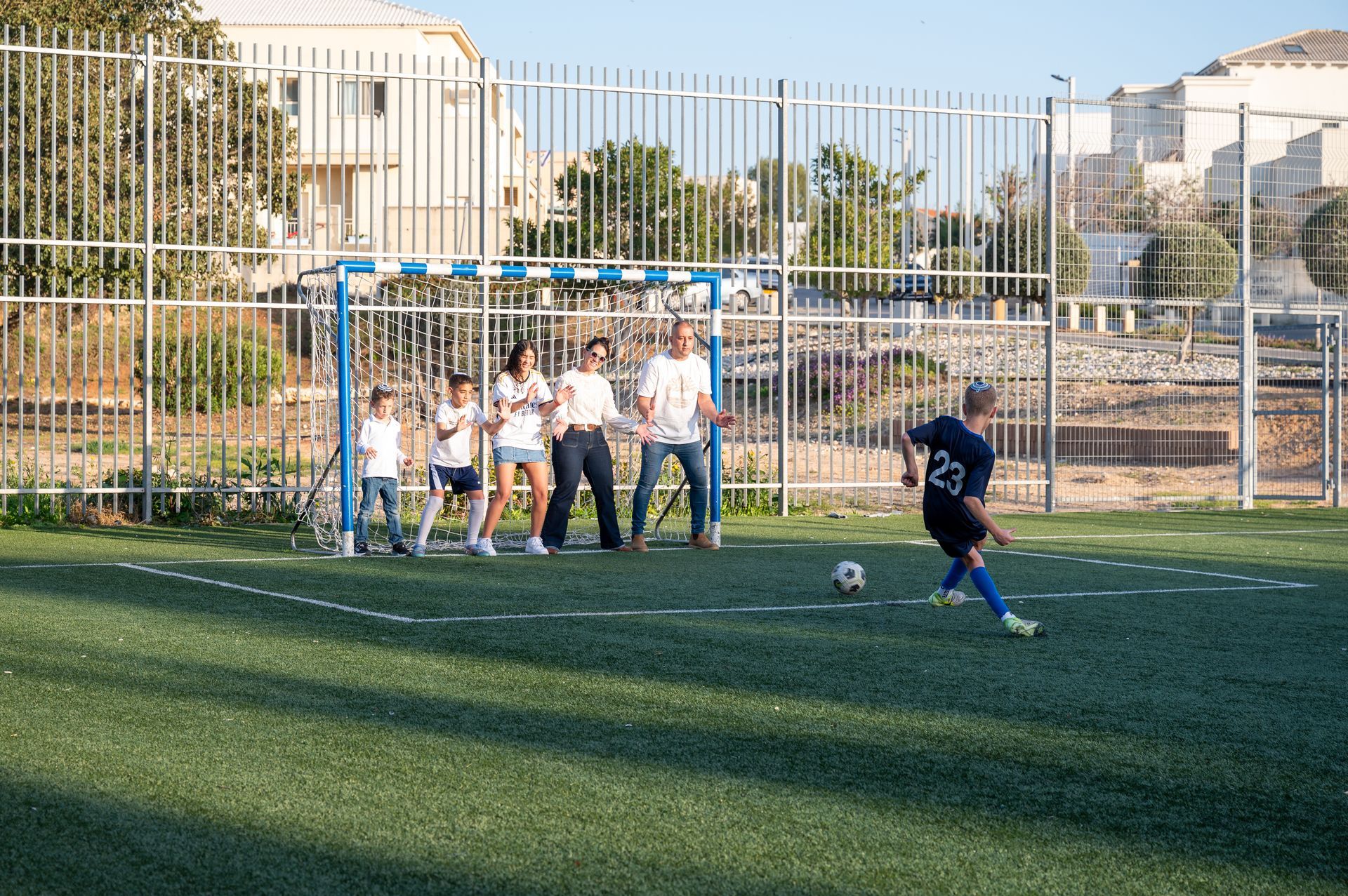 משפחה עומדת בשער וילד בר המצווה בועט כדור לעברם