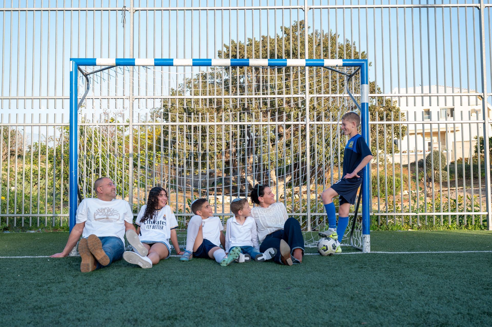 משפחה יושבת בשער כדורגל ומביטה על נער בר המצווה בצילום משפחתי
