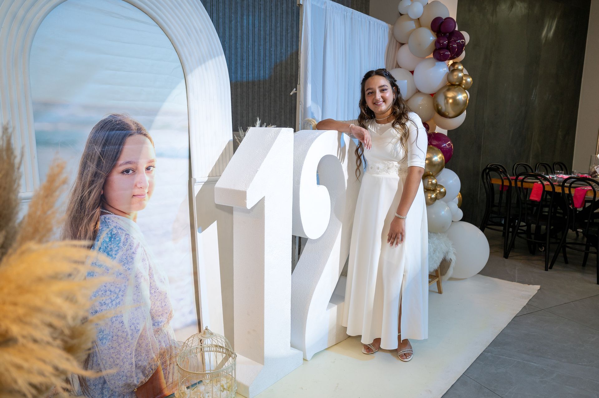 בת מצווה עדינה ומרוגשת ליד הרקע שהכינו לה באולם