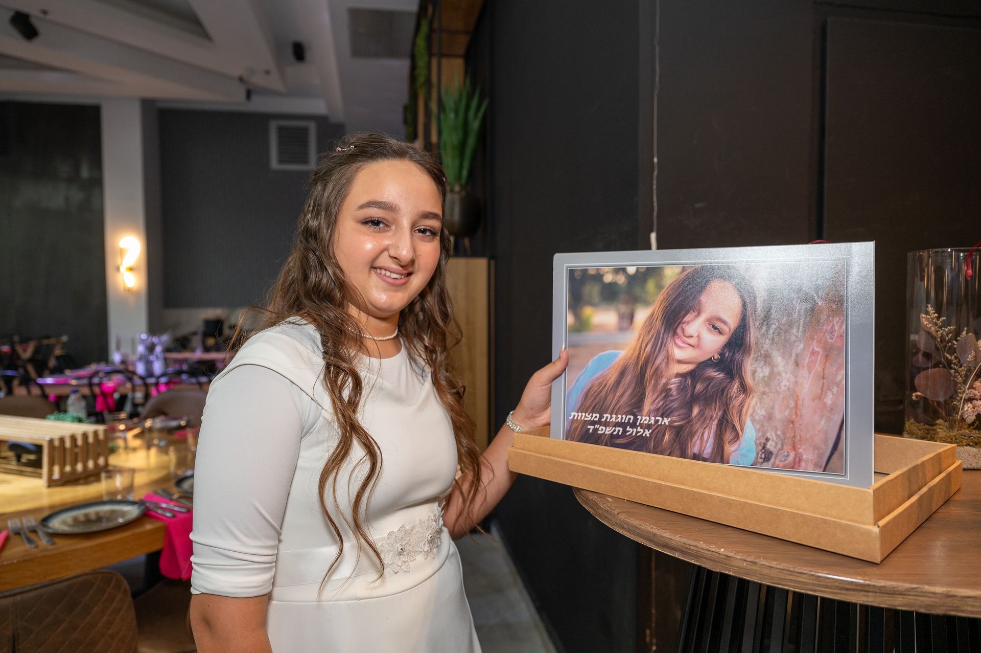 בת מצווה עדינה ומרוגשת ליד הרקע שהכינו לה באולם