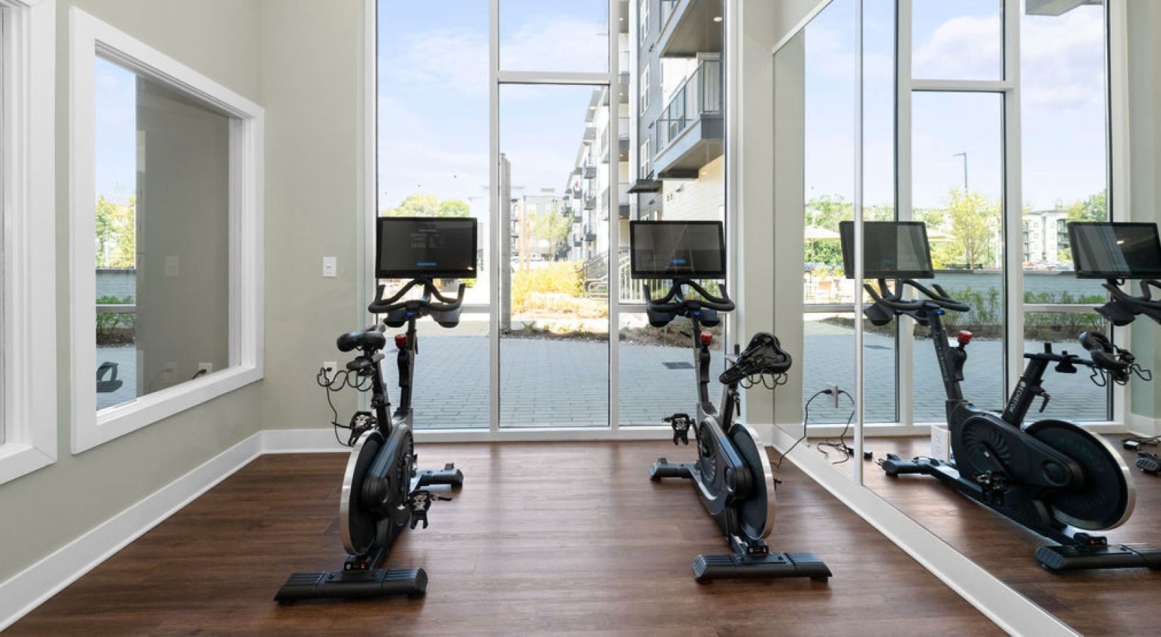 Indoor fitness center with stationary bikes and large windows overlooking courtyard.