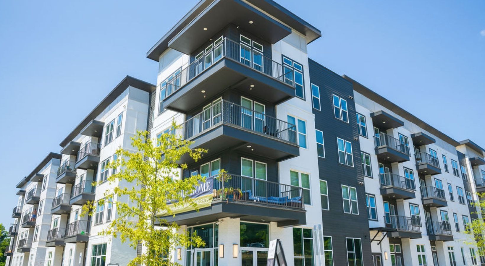 Exterior view of a modern multi-family building with balconies against a blue sky.