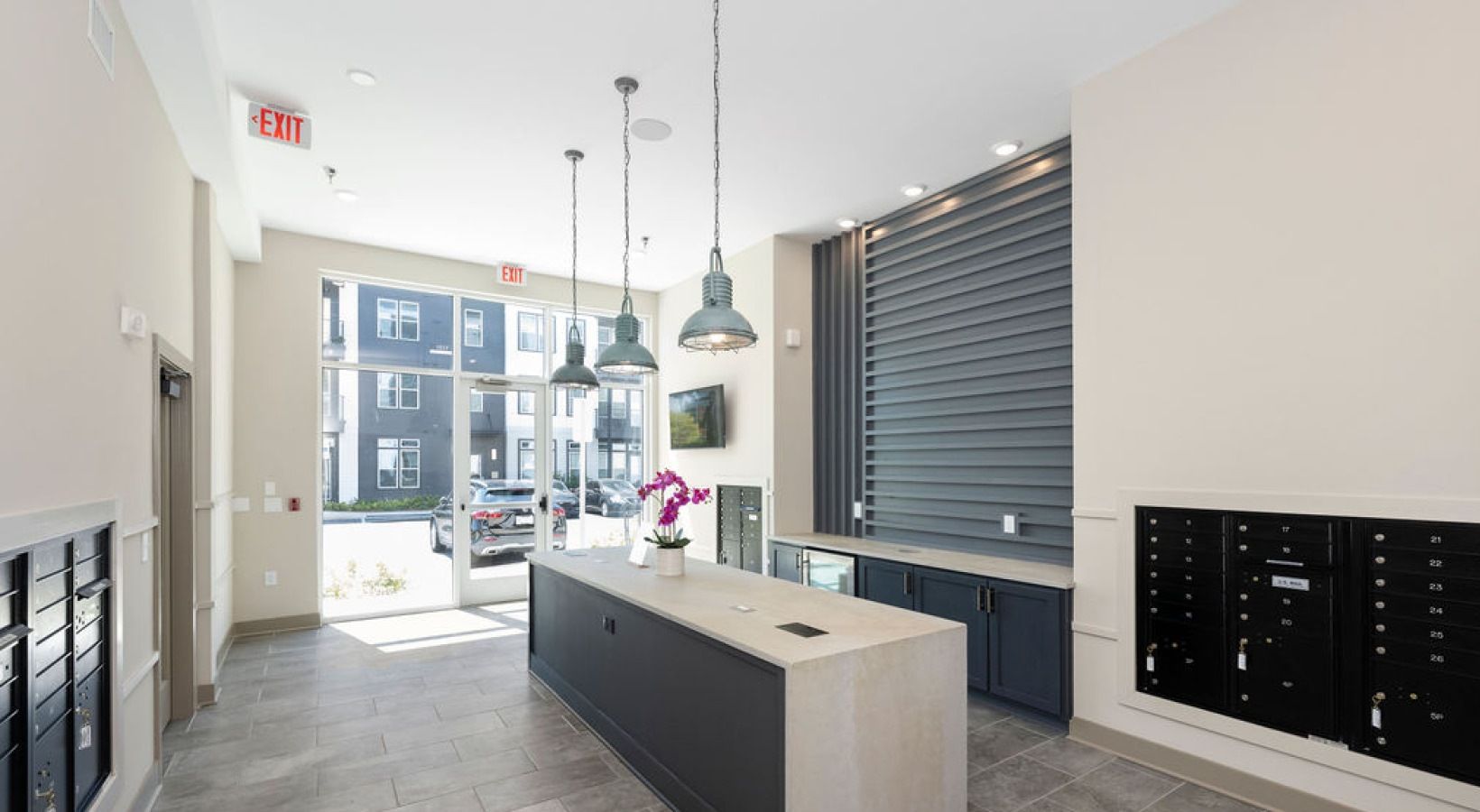 Modern apartment lobby with a reception desk, mail lockers, and large front windows.
