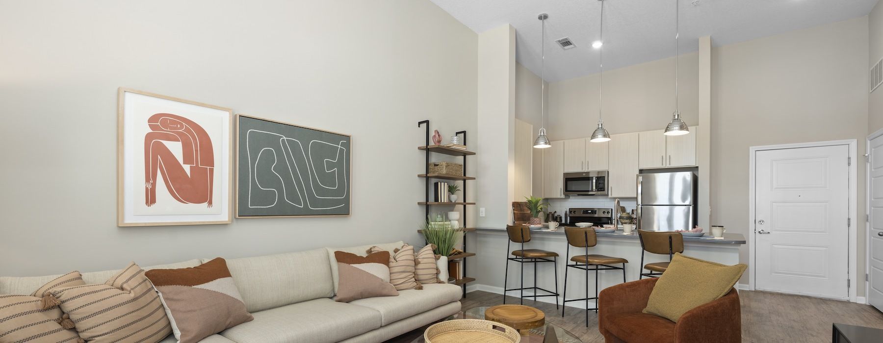 Open-concept living area with a sofa, artwork, and a kitchen with bar stools.