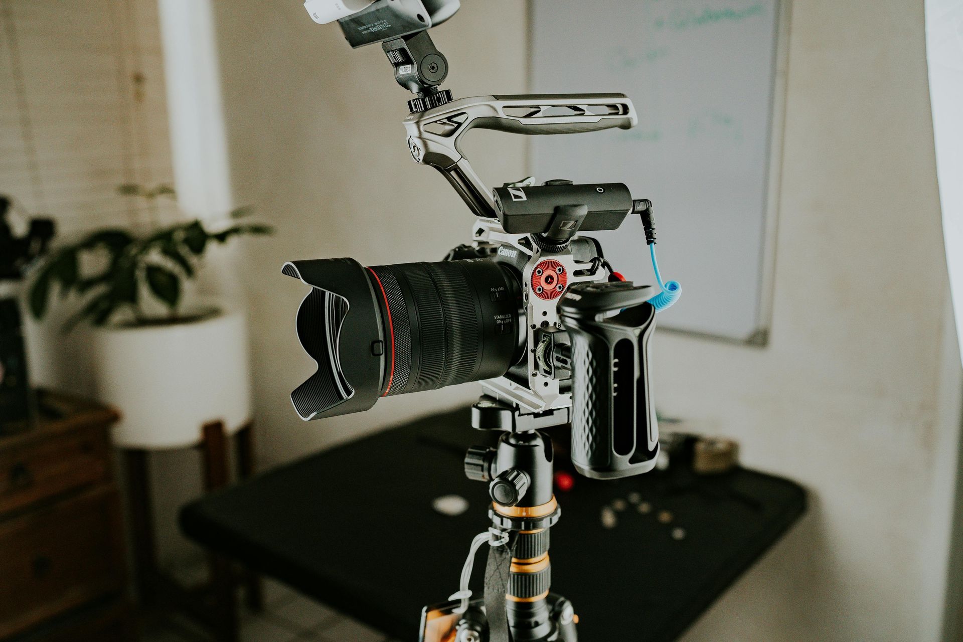 Camera setup on a tripod, with lens and accessories attached, indoors near a window and table.