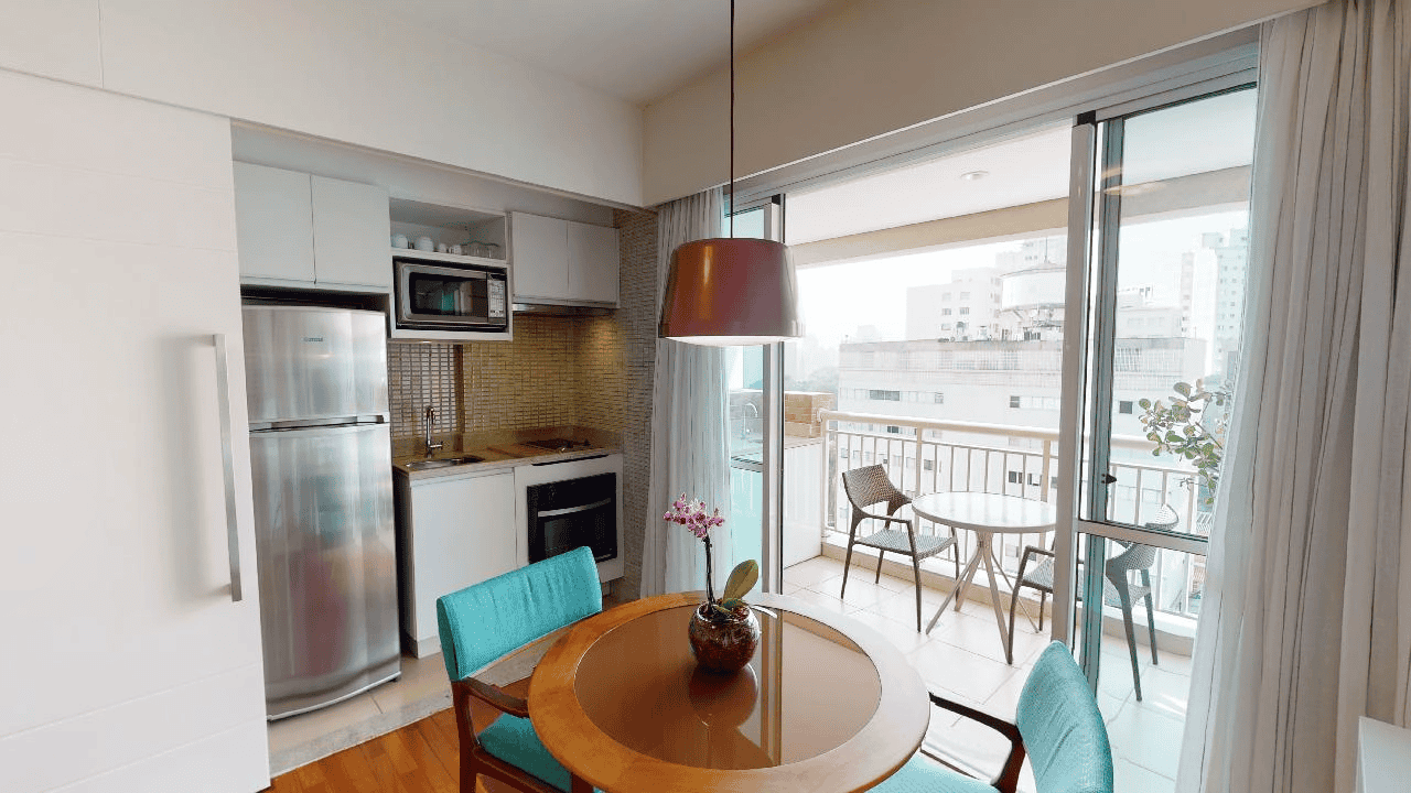 Apartamento próx. à Paulista, com Cozinha e área de jantar integrada, geladeira de aço inoxidável, mesa redonda, cadeiras.