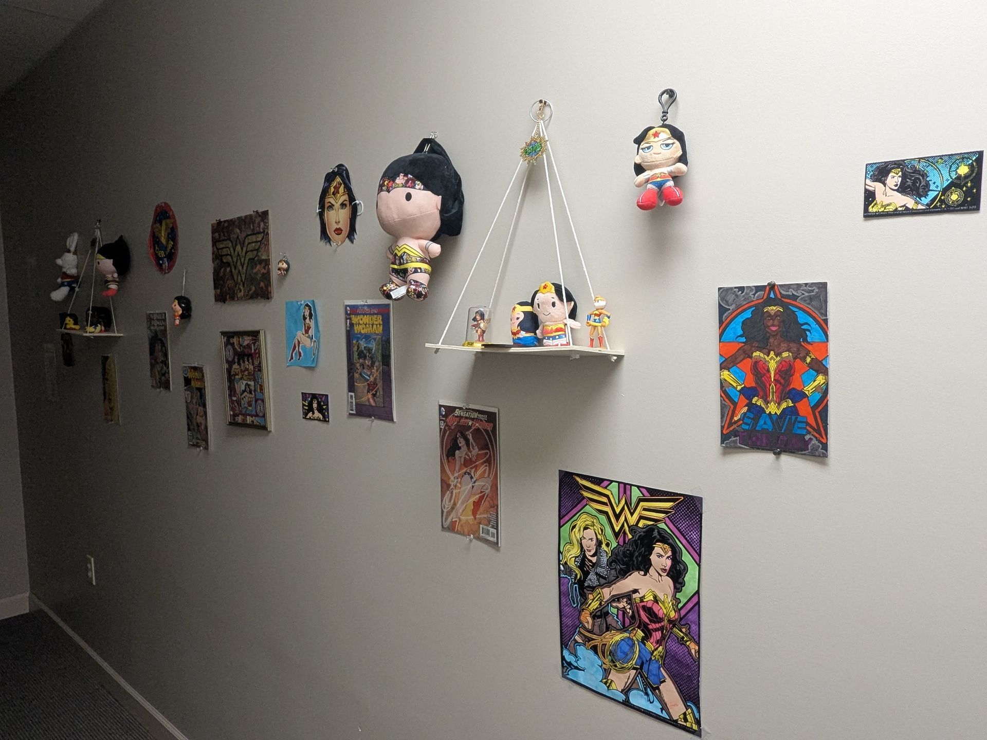 Wall display of Wonder Woman memorabilia. Art, plush toys, and shelves with figurines.