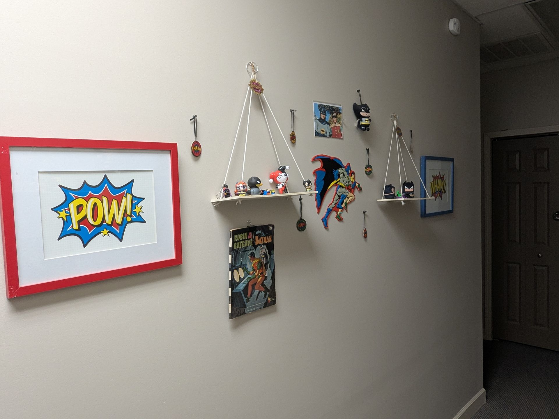 Superhero-themed wall decor in a hallway.hanging shelves with figurines, and comic book illustrations.