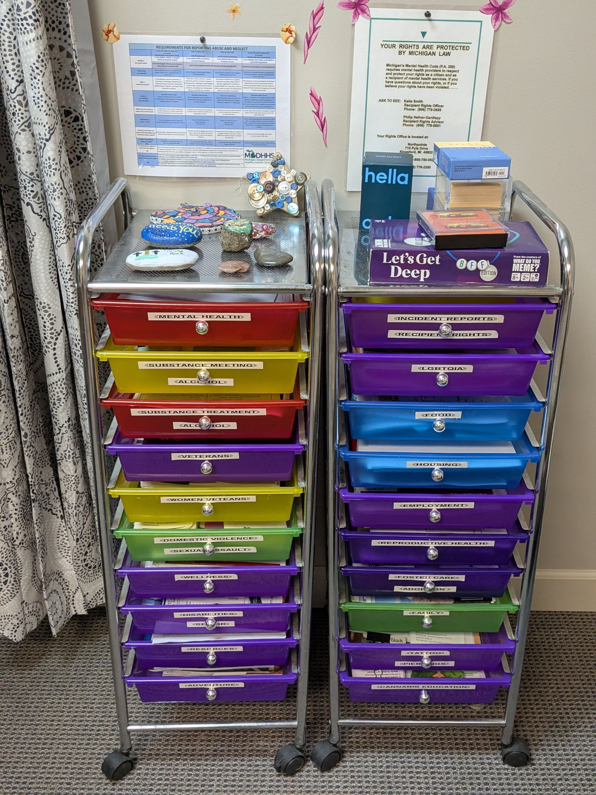 Two rolling carts with colorful bins and supplies, set against a wall with notes.
