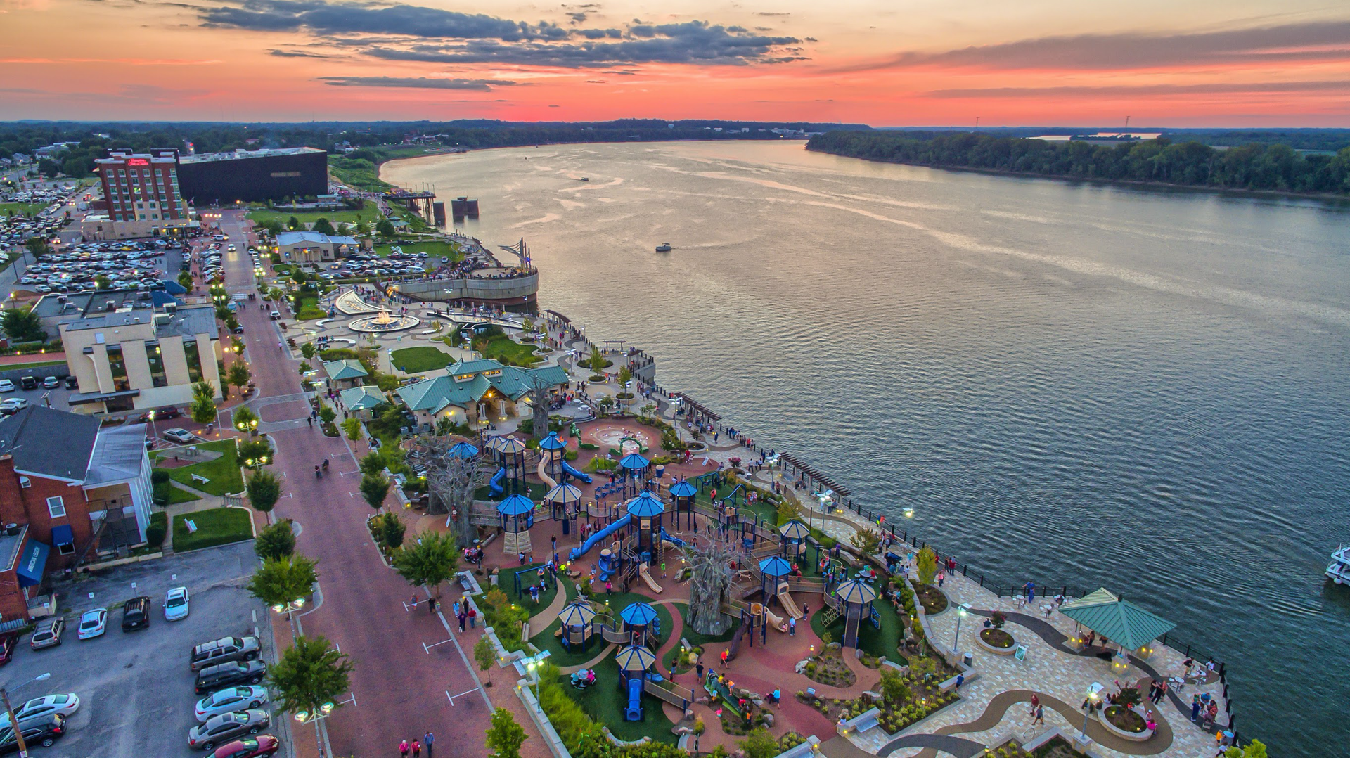 An aerial view of a park next to a river at sunset.