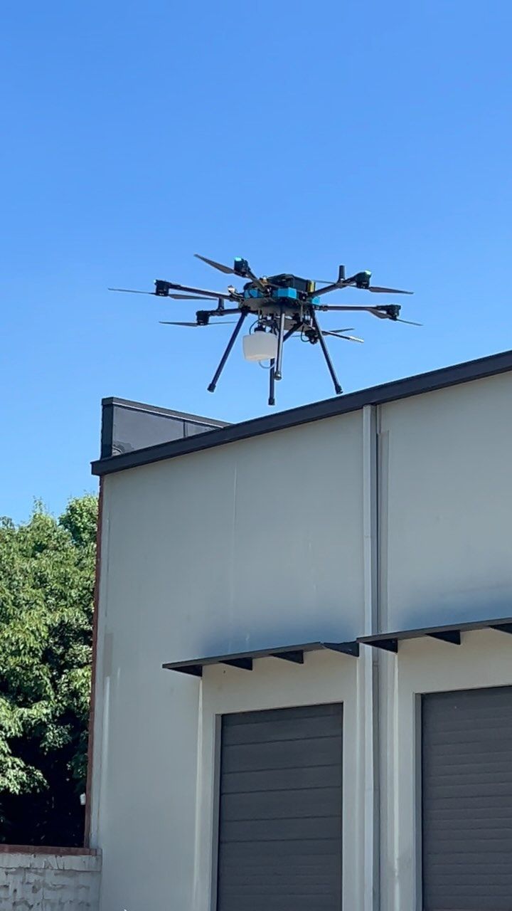 A drone is flying over a building with a blue sky in the background.