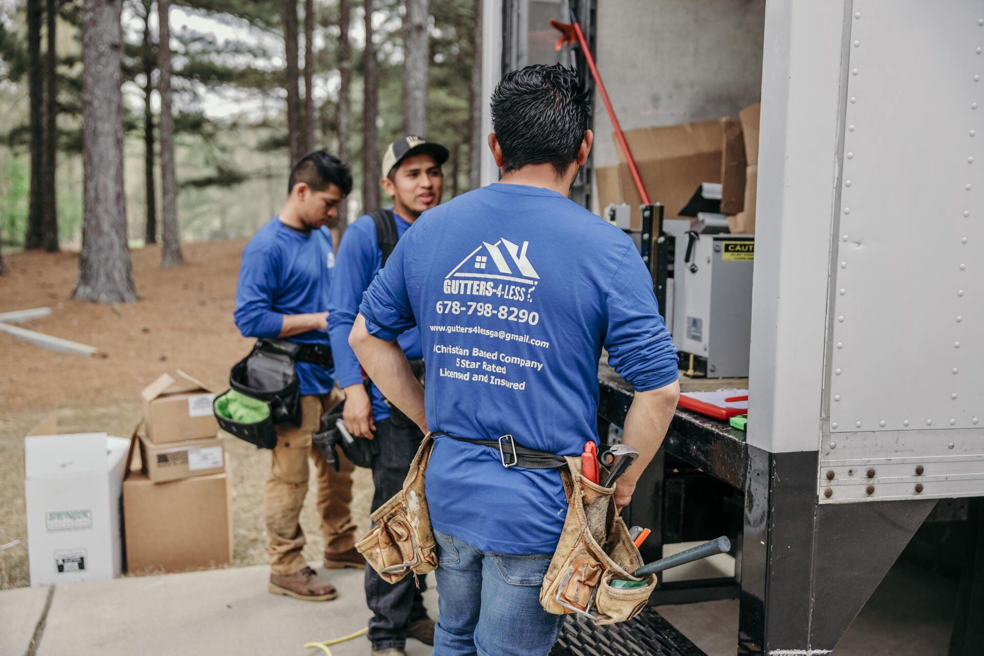 Workers in blue shirts loading tools beside a truck at a wooded construction site