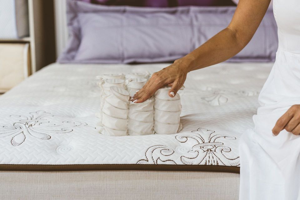 Woman's hand touches exposed mattress springs on a bed with lavender pillows.