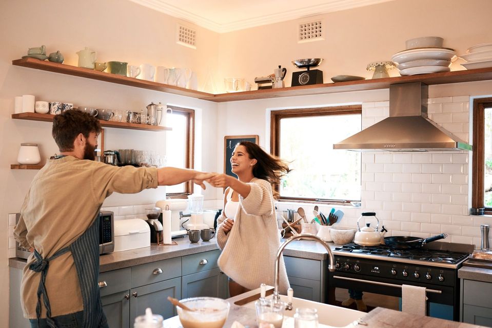 Couple dancing in a bright kitchen. She's smiling, he's wearing an apron.