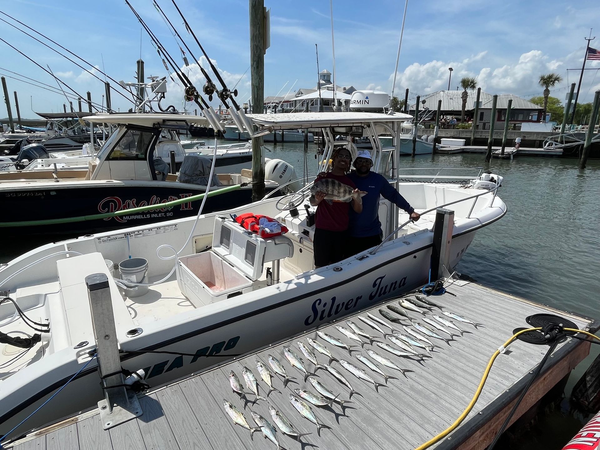 Two people on a boat at a dock with fish lined up. 