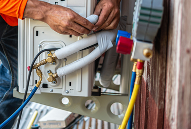 A technician repairs an outdoor air conditioning unit, using pressure gauges and insulated refrigerant lines.