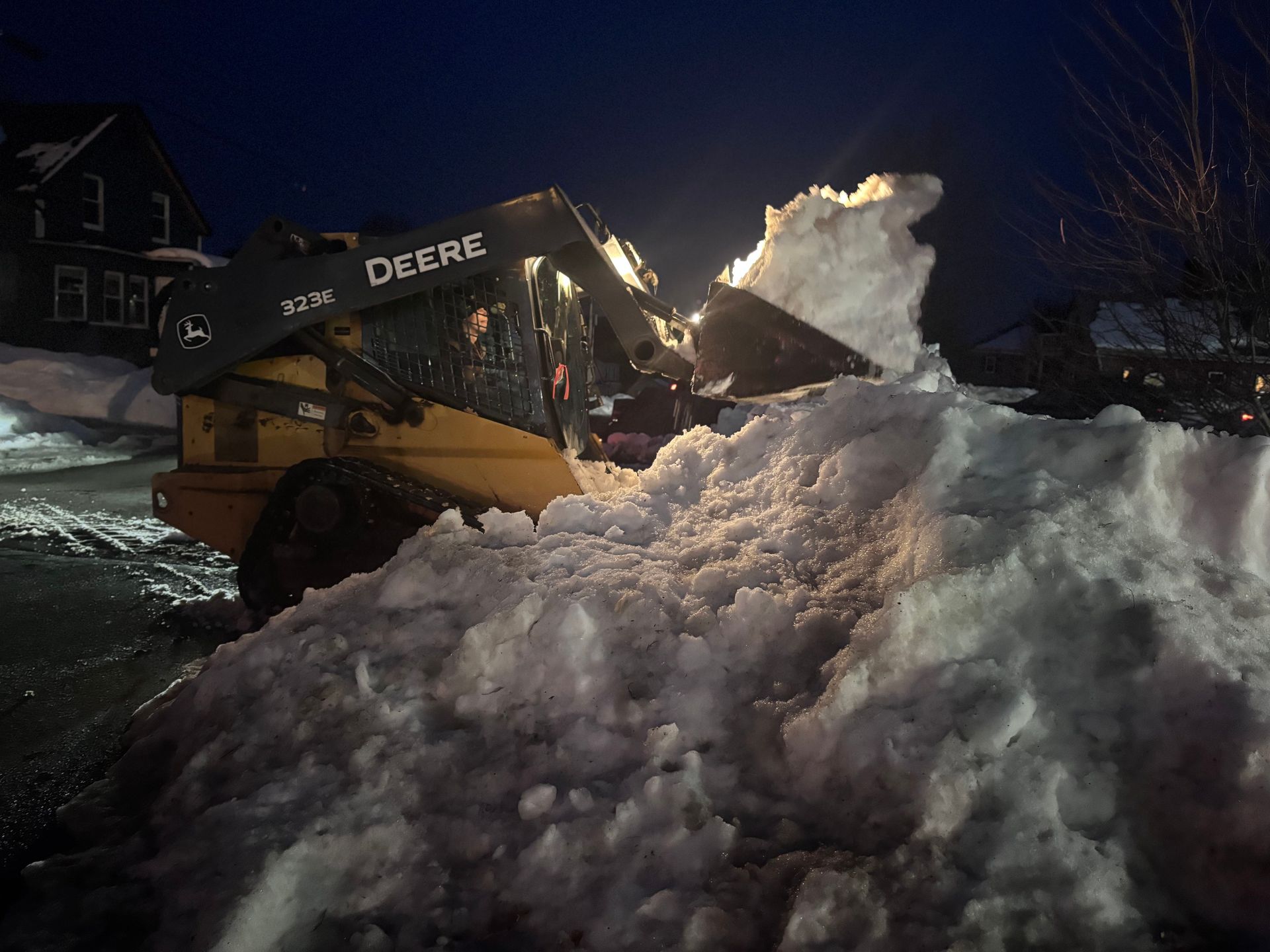 Yellow John Deere skid-steer loader plowing snow at night.