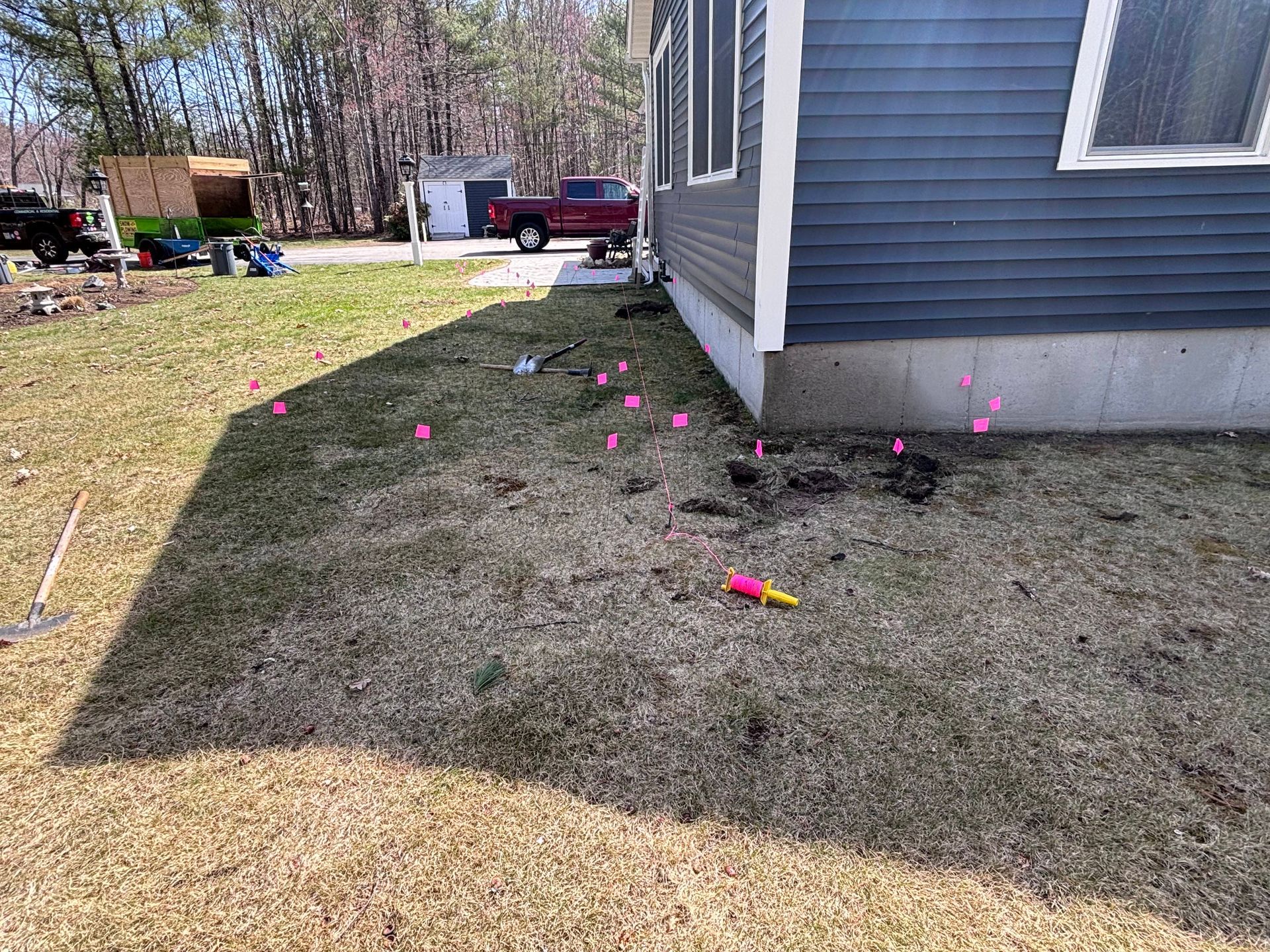 Lawn with pink flags near a blue house. A red truck is parked in the distance.