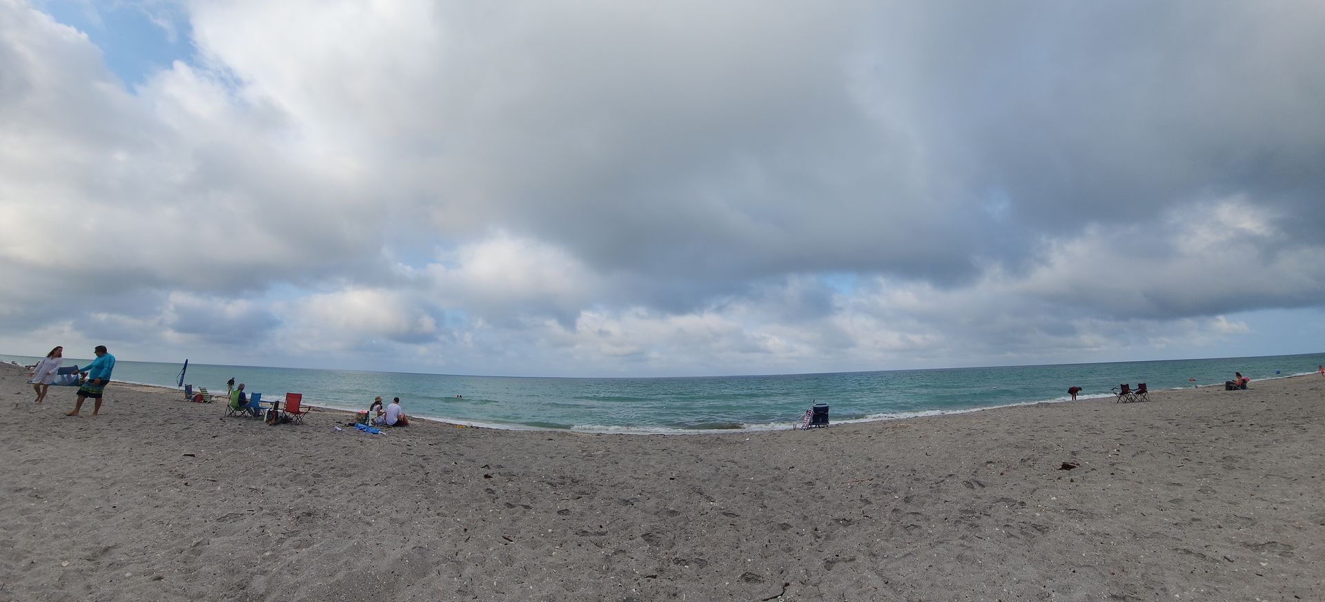 Cloudy beach scene with people scattered along the shore and turquoise water in the background