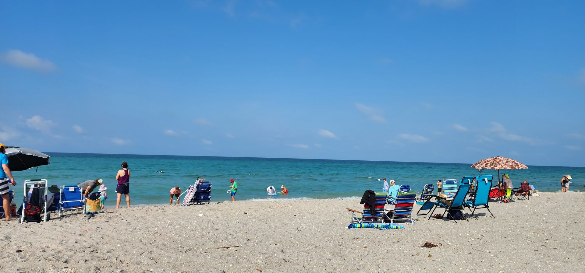 Sunny beach with people on chairs under umbrellas beside calm blue ocean