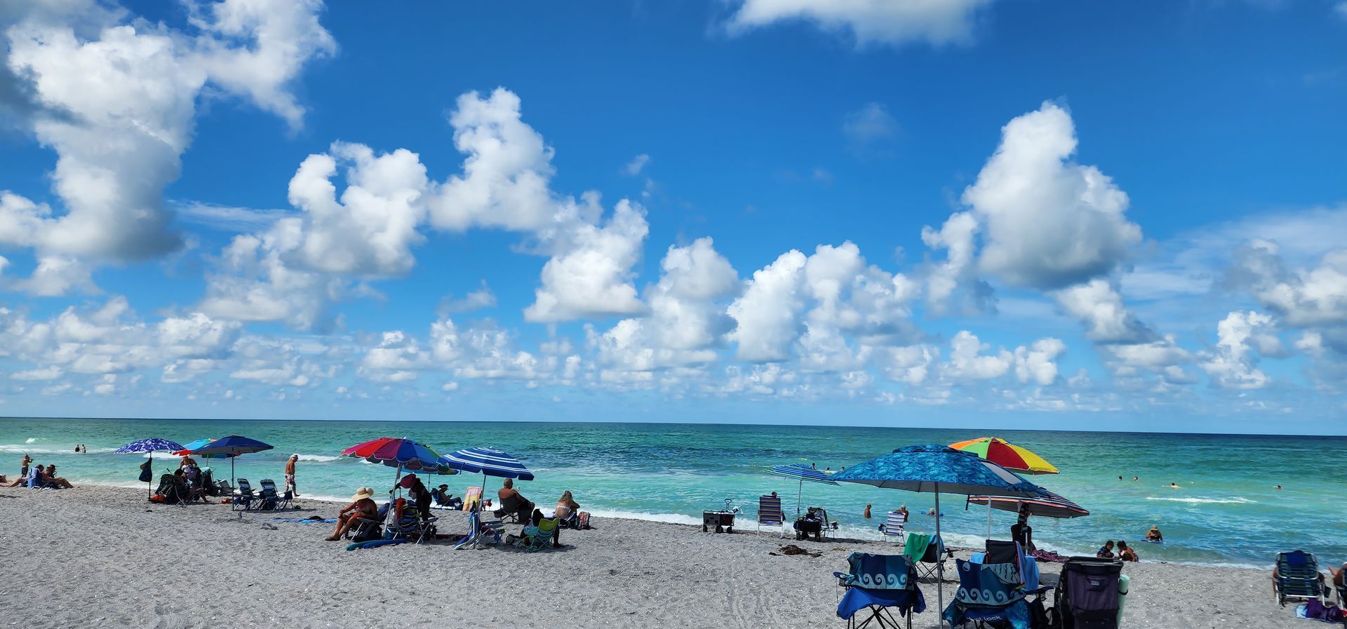 Sunny beach with people under colorful umbrellas beside turquoise water and a blue sky with clouds
