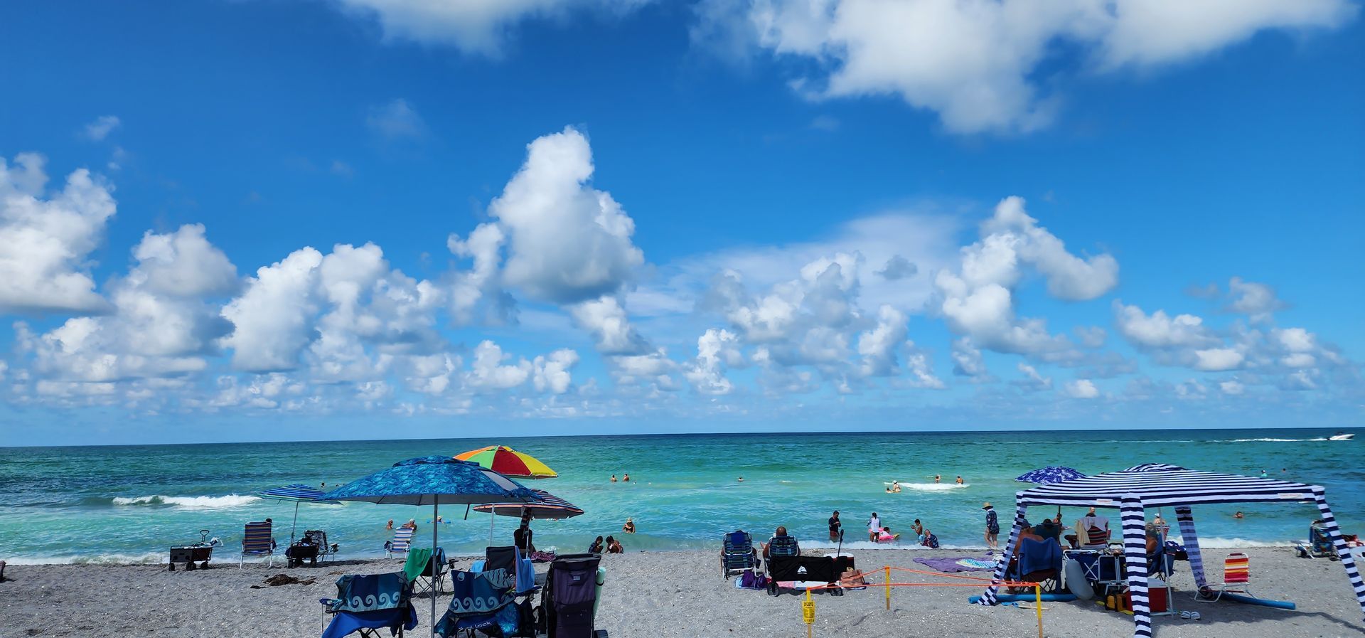 Sunny beach with turquoise water, umbrellas, and people relaxing under a bright blue sky