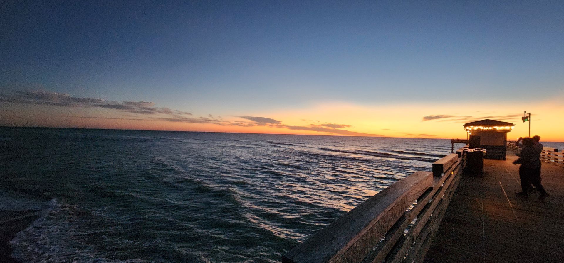 Sunset over ocean beside a ship deck, with waves and orange sky
