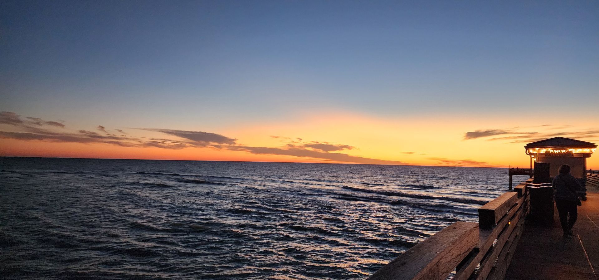 Sunset over the ocean with waves and a silhouetted pier