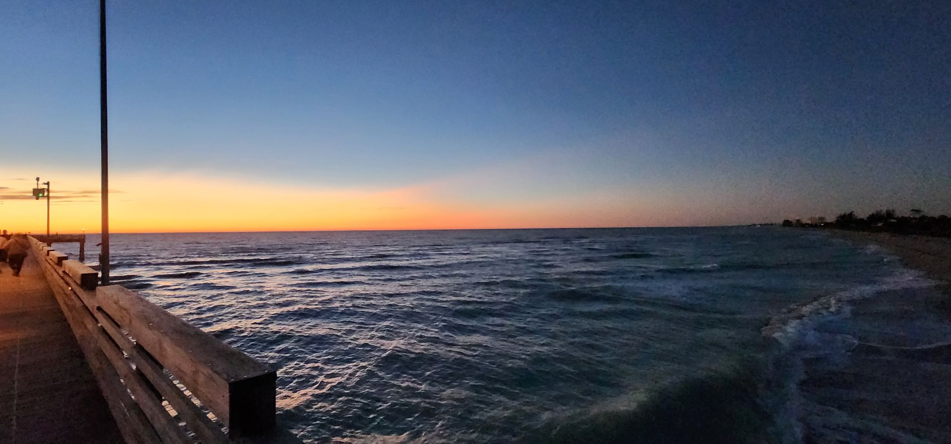 Sunset over choppy ocean beside a wooden pier and railing