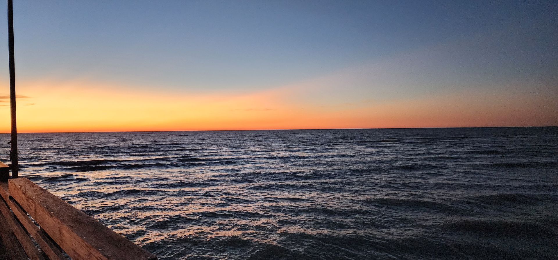 Sunset over choppy ocean with a wooden pier at left