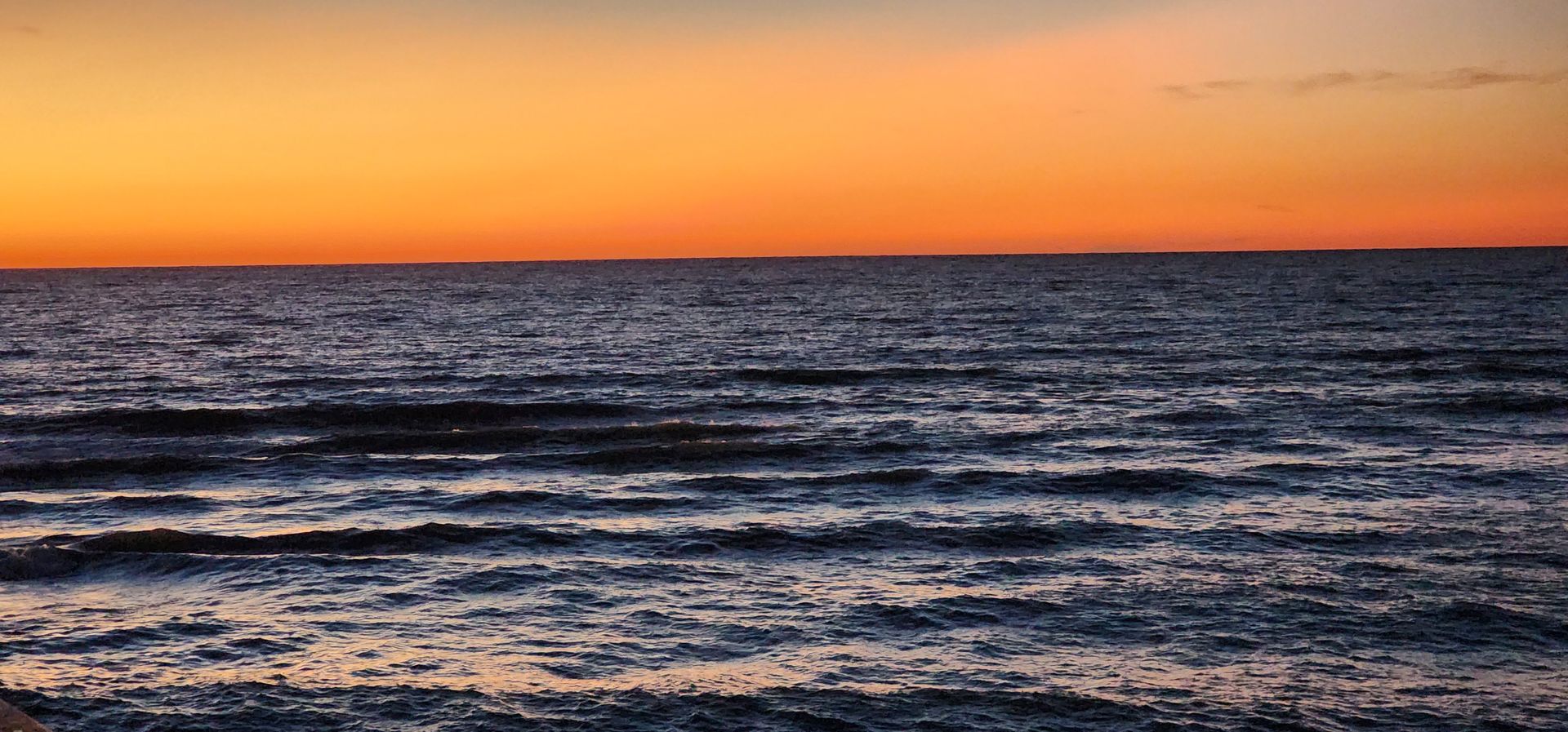 Sunset over a calm ocean with orange sky and dark waves